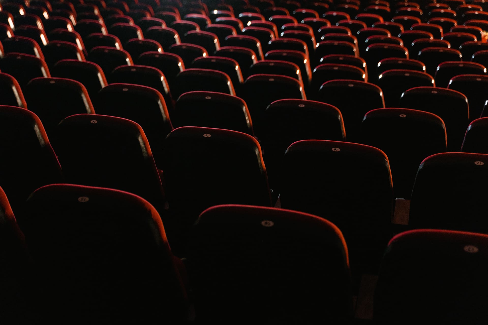 Poltrone di una vecchia sala cinematografica al buio, attraversate dal fascio di luce del proiettore
