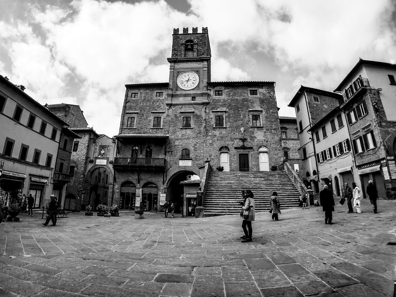 Banchi del mercato sotto i tendoni bianchi in una piazza in pietra del centro storico di Cortona