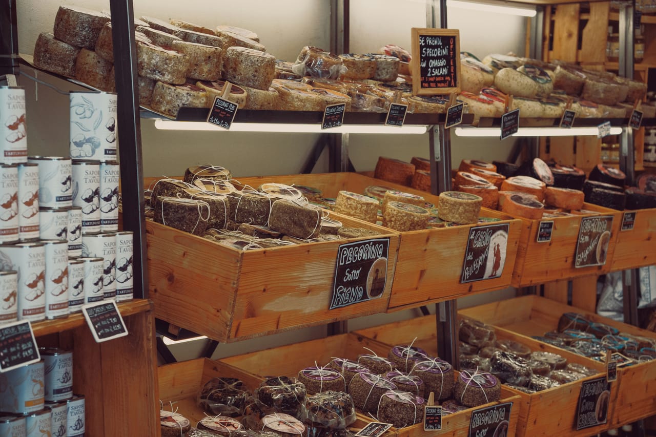 Forme di pecorino stagionato e salumi toscani esposti sul bancone di un banco del mercato