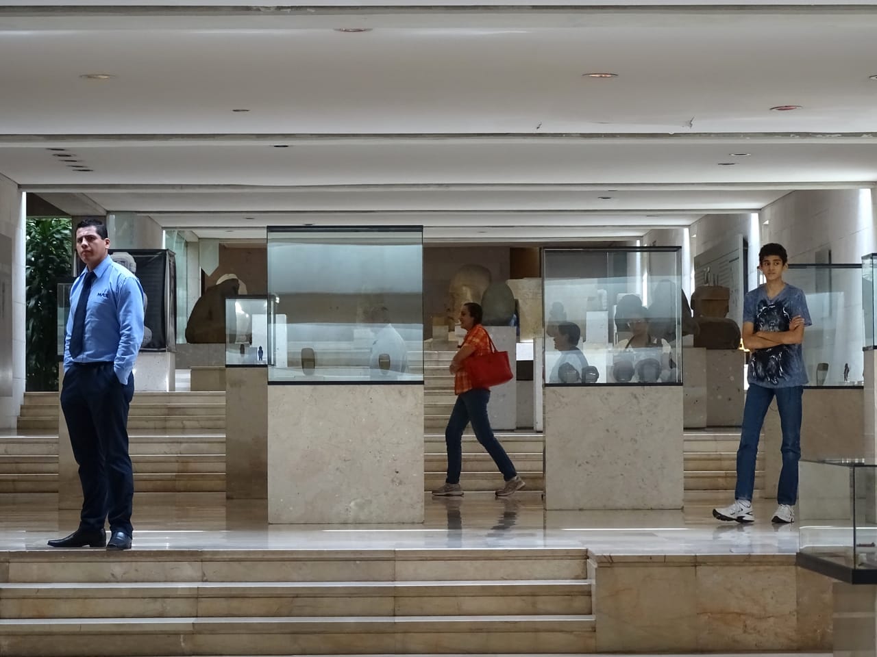Visitors walk through the rooms of an art museum with paintings hanging on the walls.