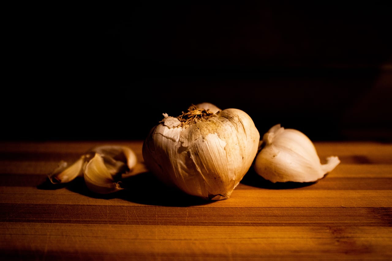 Bulbi di aglione della Valdichiana a confronto con l'aglio comune su un tagliere di legno